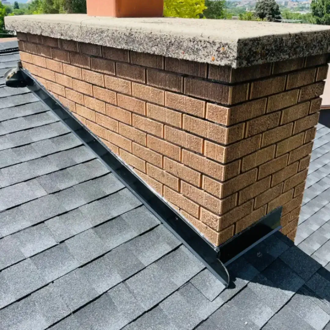 Brick chimney with cap on a gray shingle roof, with flashing visible.