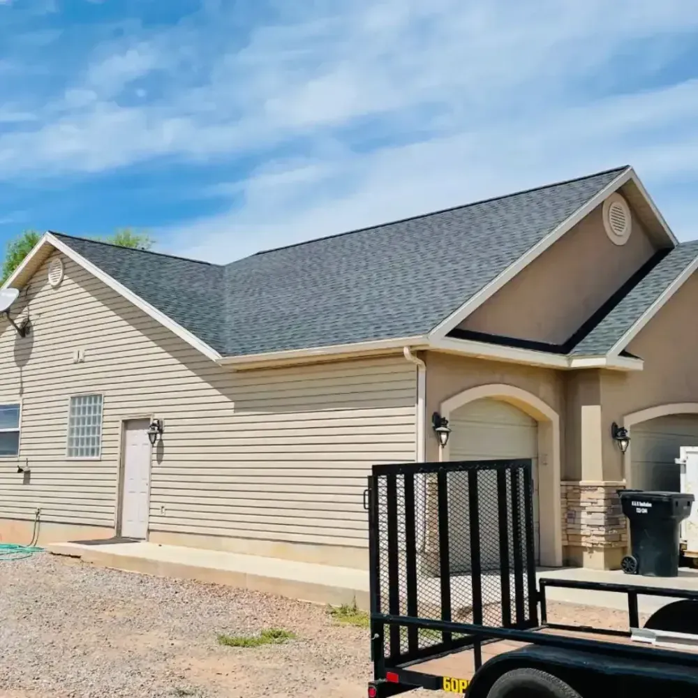 Beige house with gray roof, two-car garage, and black trailer in front.