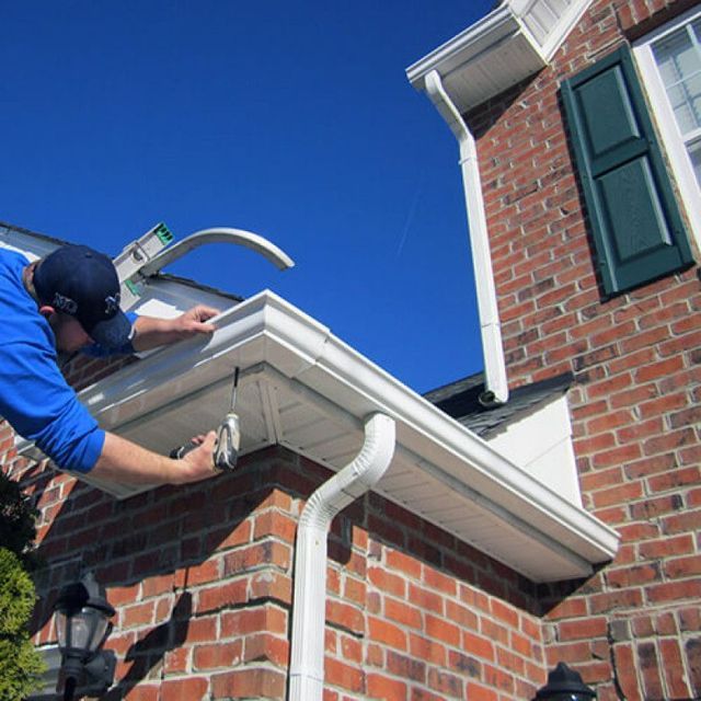Roofers working on a shingled roof, with parked vehicles and a street in the background.