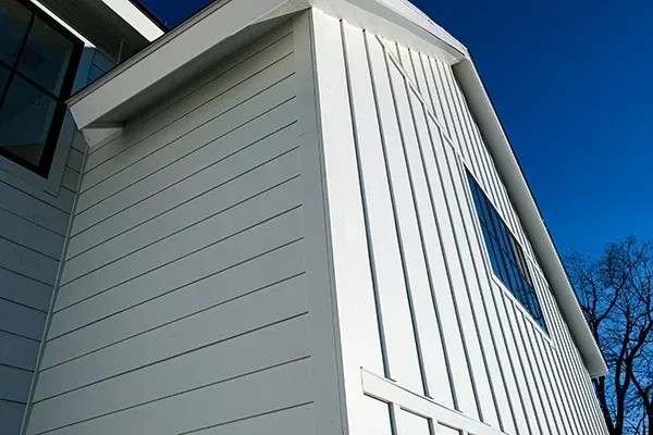 White siding on a modern building with vertical and horizontal lines under a blue sky.
