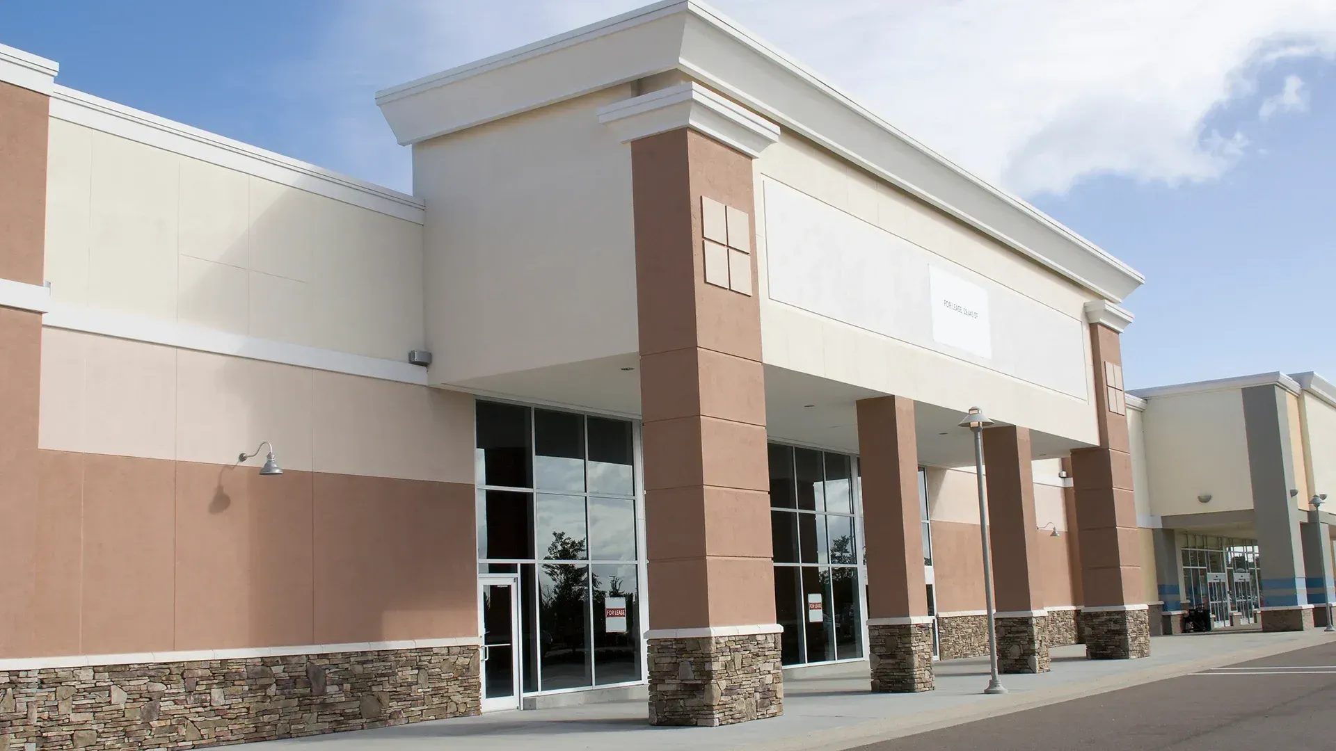 Exterior of a vacant commercial building with large glass windows and brown columns.