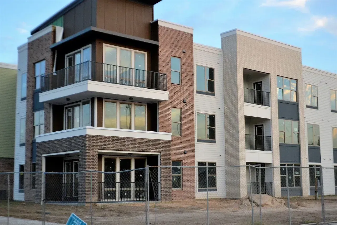 Multi-story modern apartment building under construction, brown and white brick, metal balconies.