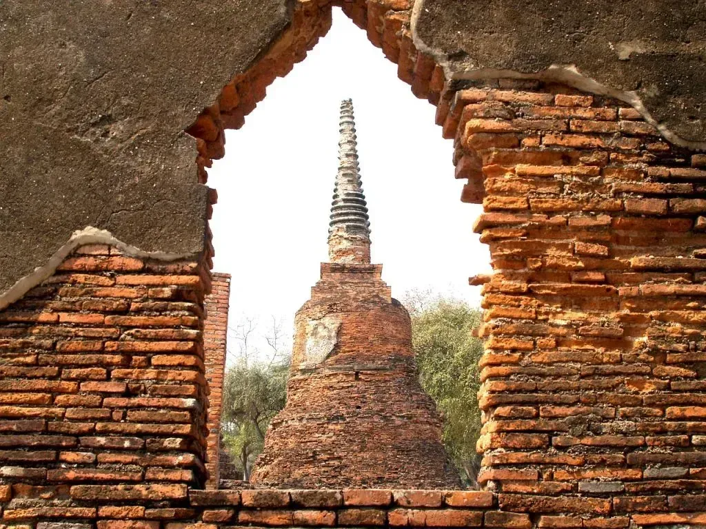 Old brick structure framing a view of an ancient temple spire in Thailand.