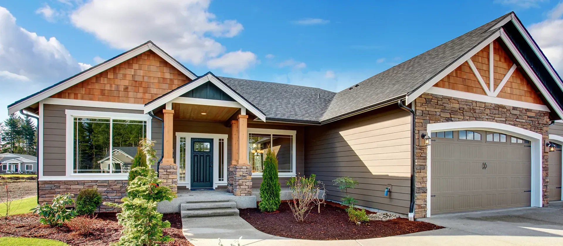 Two dormer windows with wood frames on a slate roof under a blue sky.