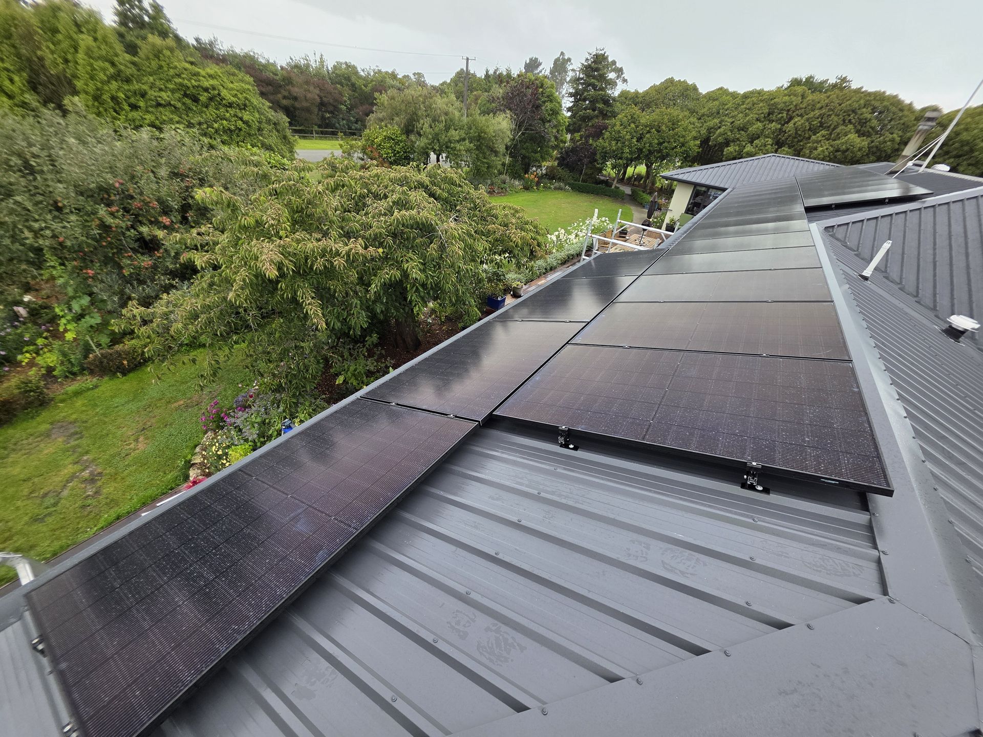 Solar panels on a gray metal roof with greenery in the background. Overcast day.