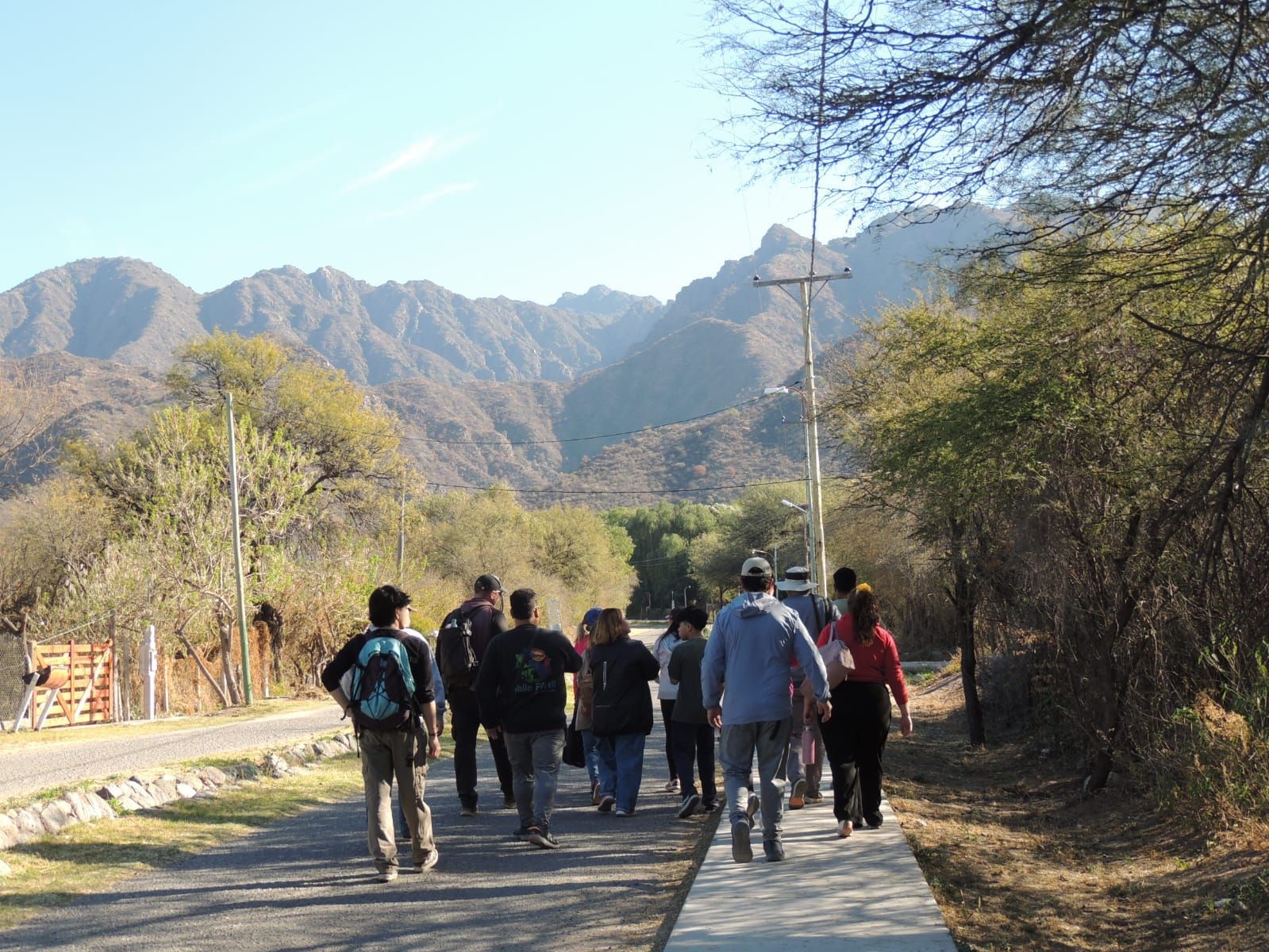 Grupo caminando por un sendero con montañas al fondo bajo un cielo despejado.
