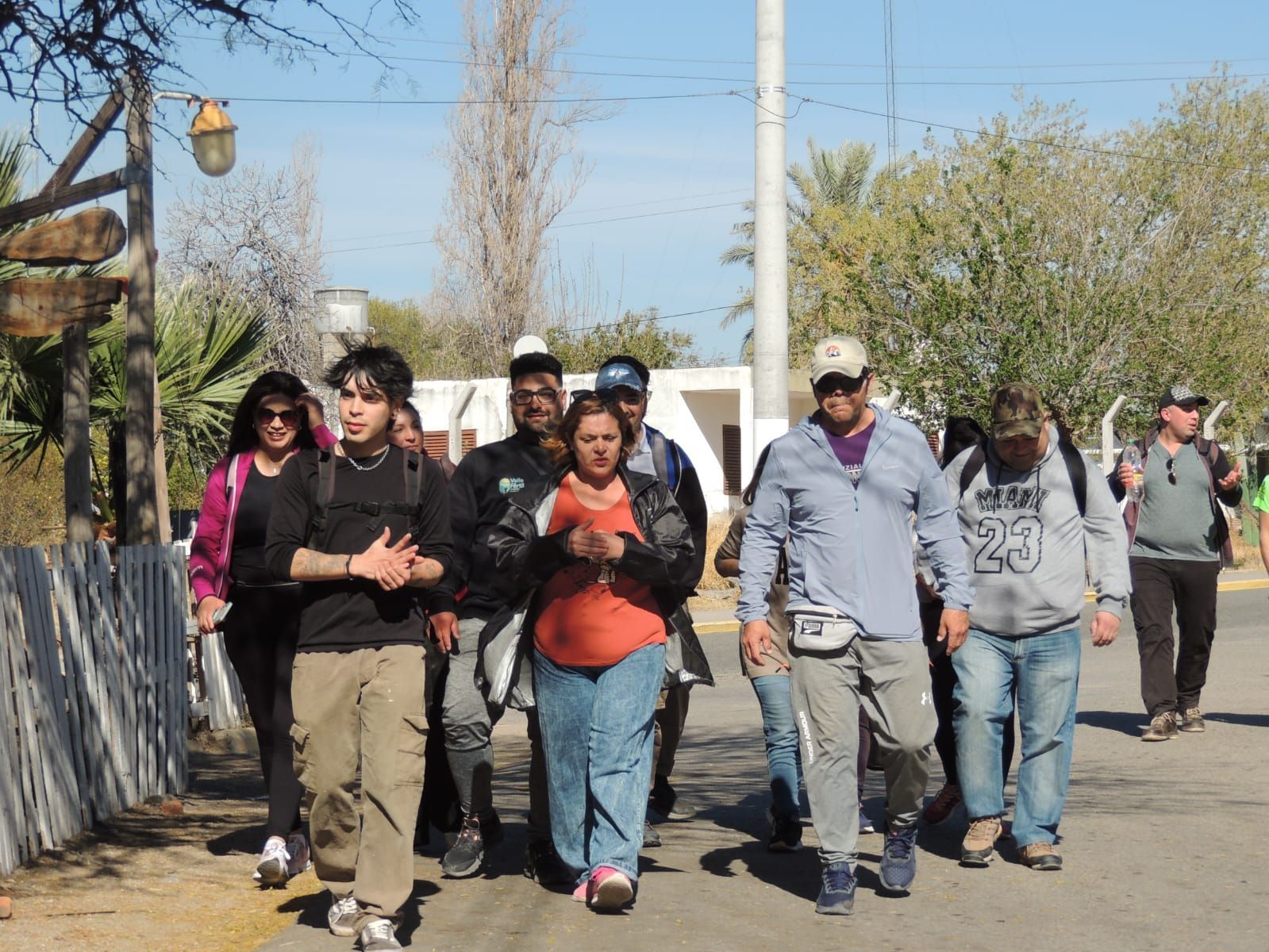 Grupo de personas caminando por un sendero, en un entorno soleado al aire libre.