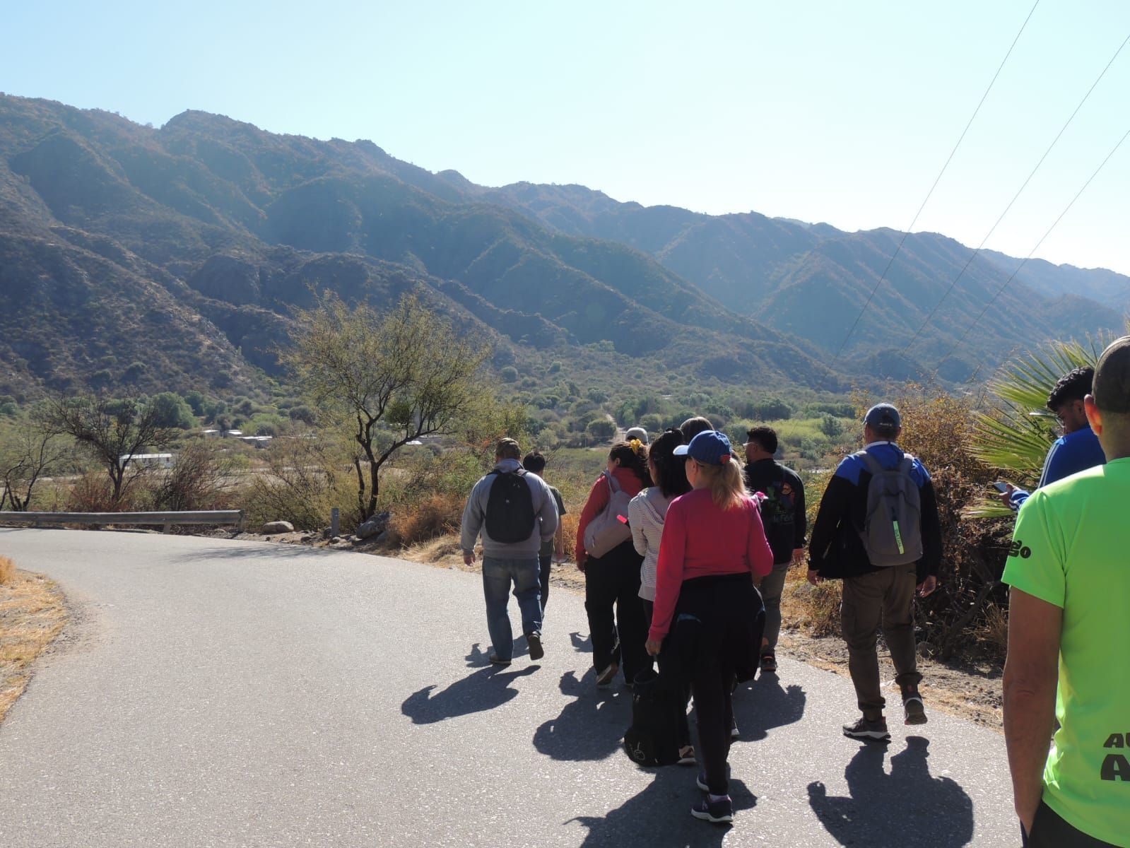 Grupo de personas caminando por una carretera con montañas al fondo bajo un cielo despejado.