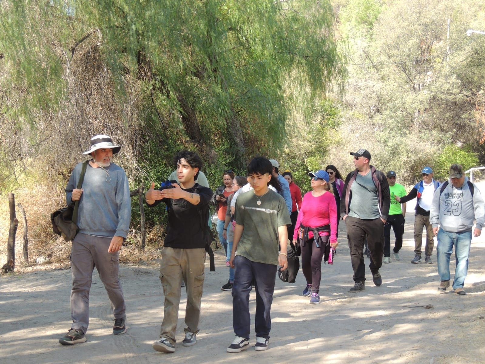 Grupo de personas caminando por un sendero de tierra en una zona boscosa en un día soleado.