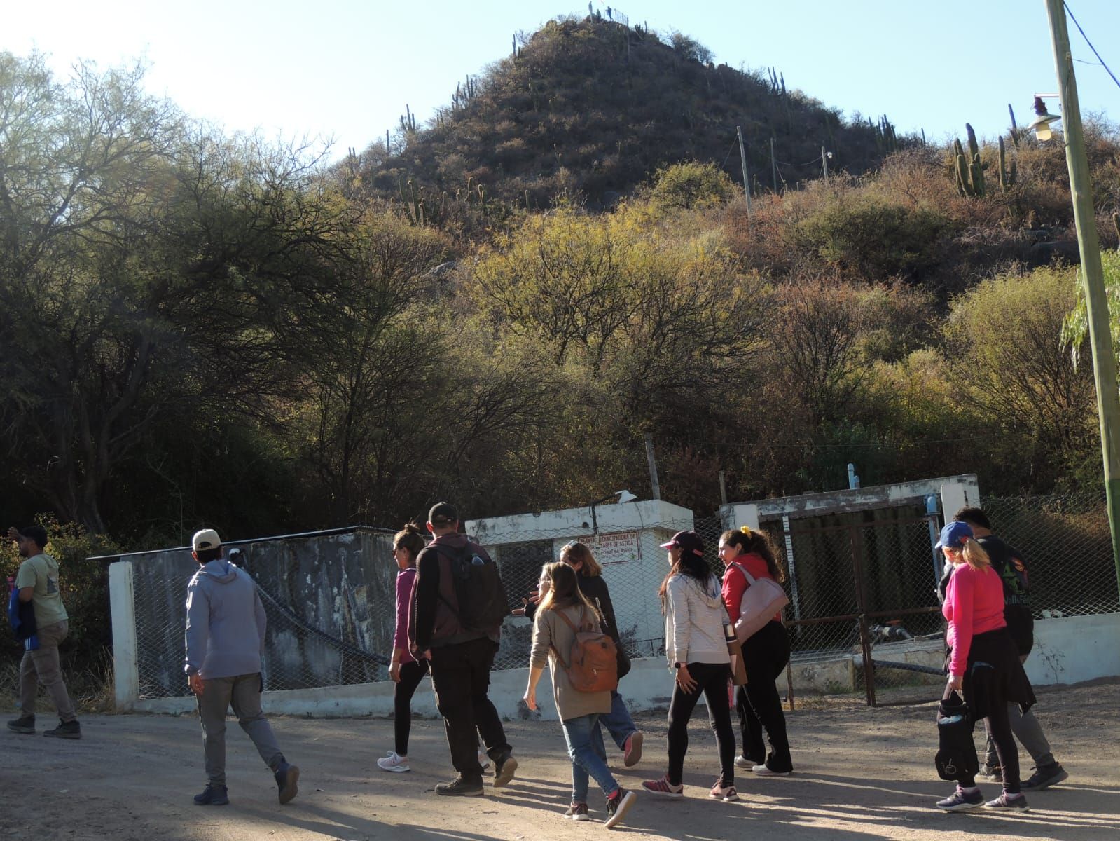 Grupo de personas caminando por una carretera con una colina al fondo.