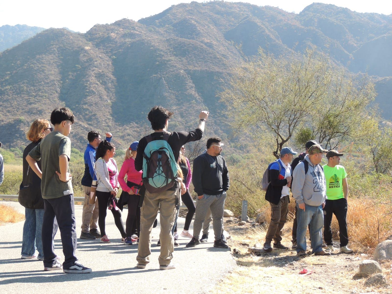 Grupo de personas haciendo senderismo al aire libre, señalando una cadena montañosa en un día soleado.