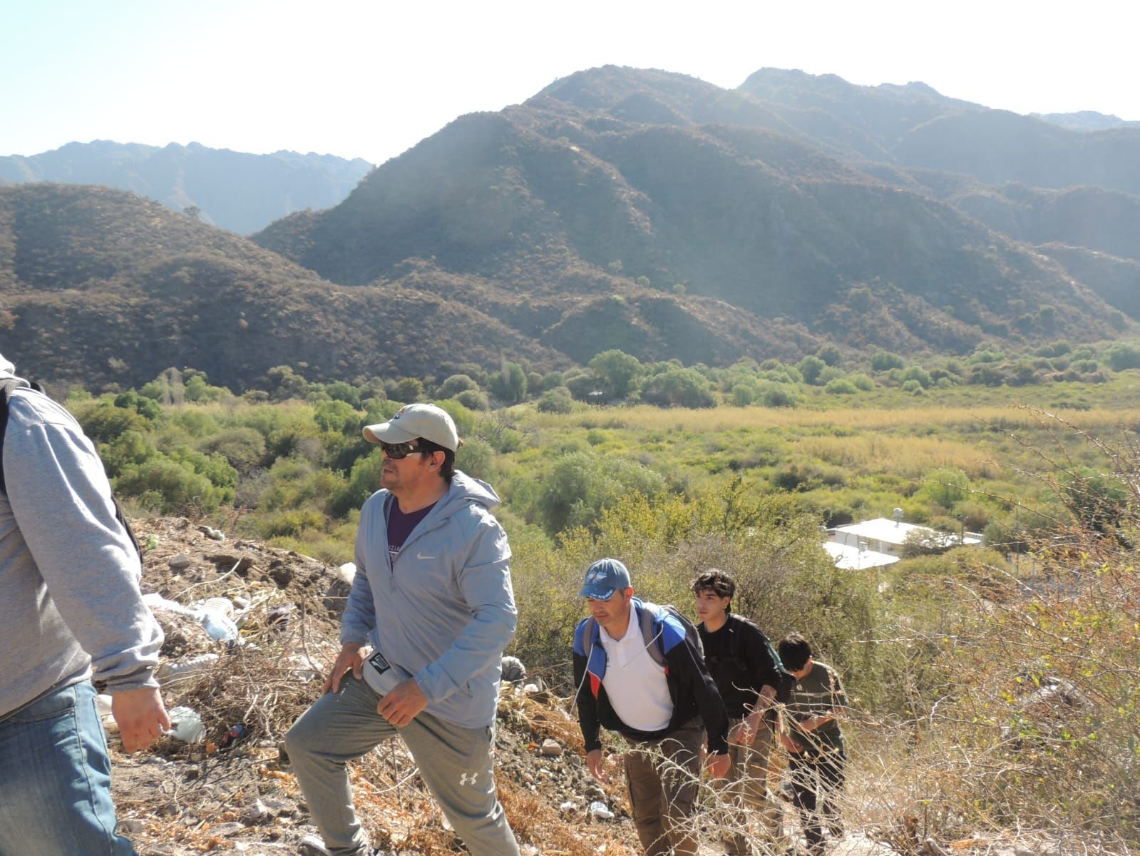 Excursionistas ascendiendo por un sendero seco y rocoso hacia una montaña, día soleado.