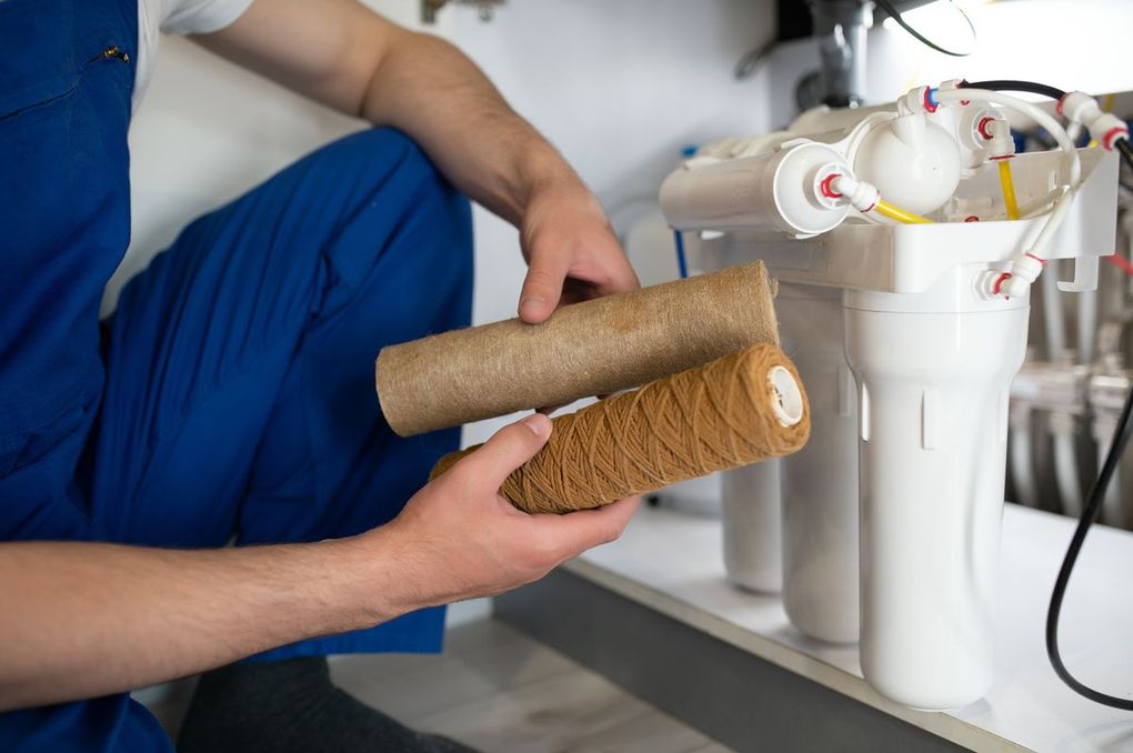 A man is fixing a water filter in a kitchen.