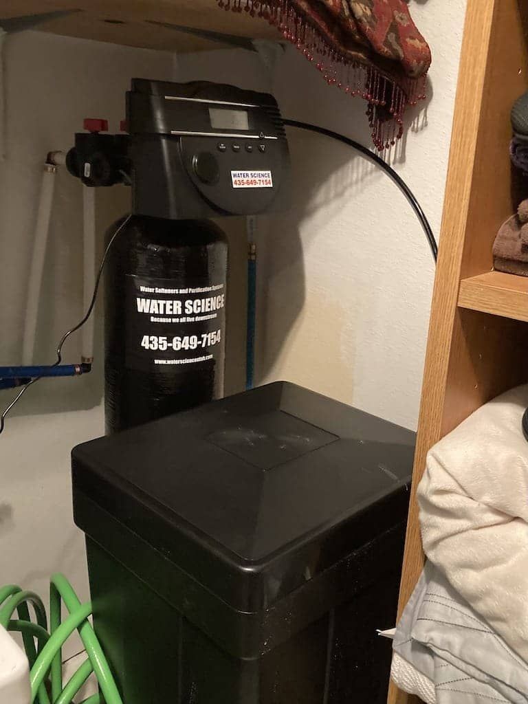 A water softener is sitting in a closet next to a shelf.