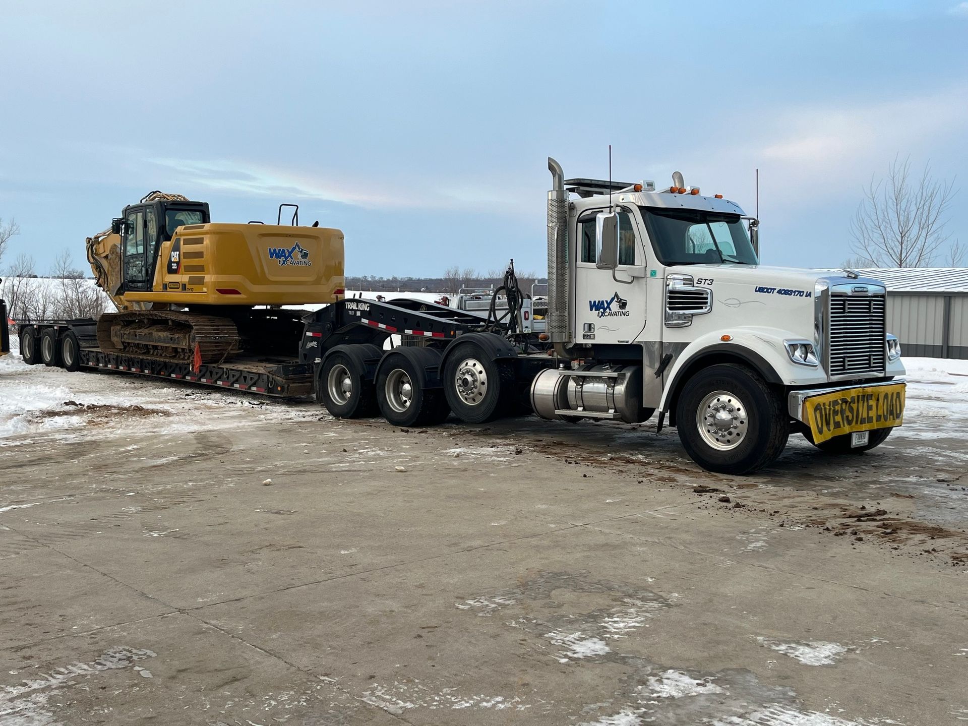 A white semi truck is carrying a yellow excavator on a trailer.