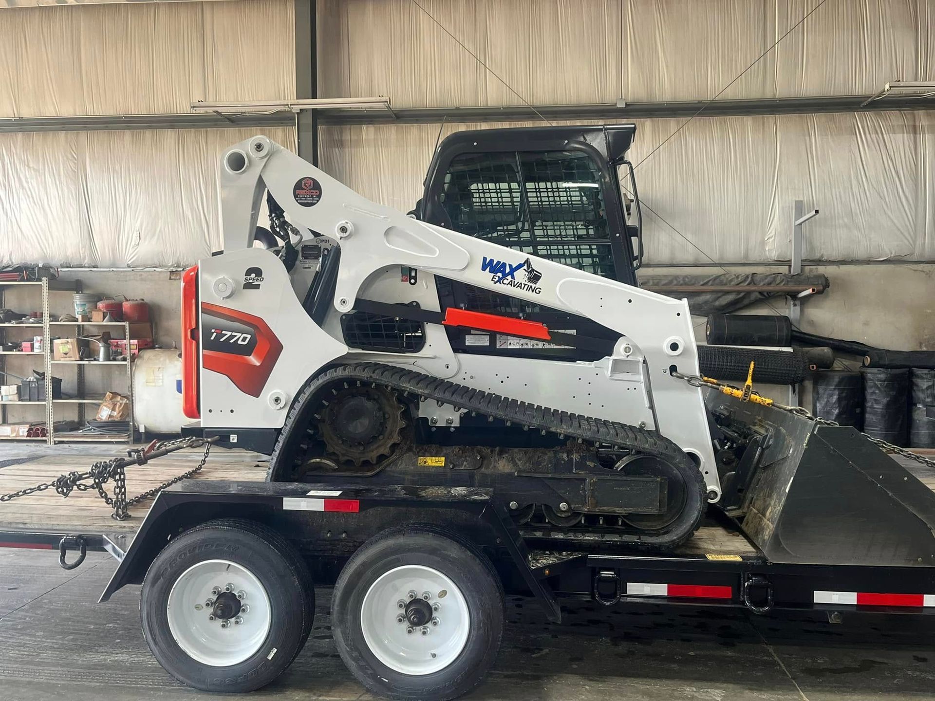 A bobcat is sitting on top of a trailer in a garage.