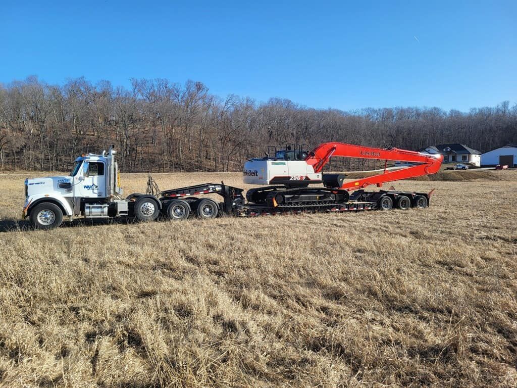 A semi truck is carrying an excavator on a trailer in a field.