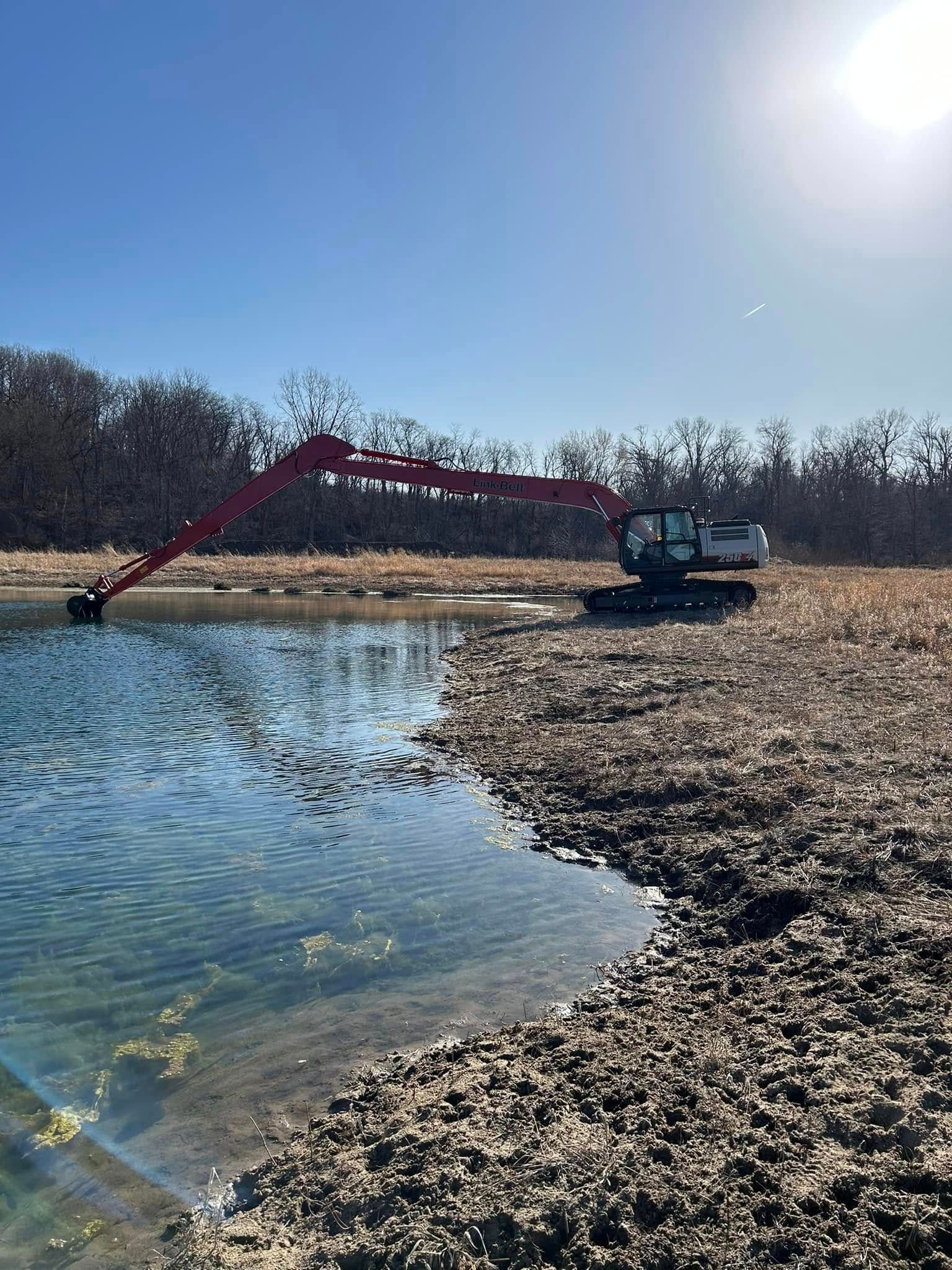 A red excavator is digging a pond in the middle of a field.