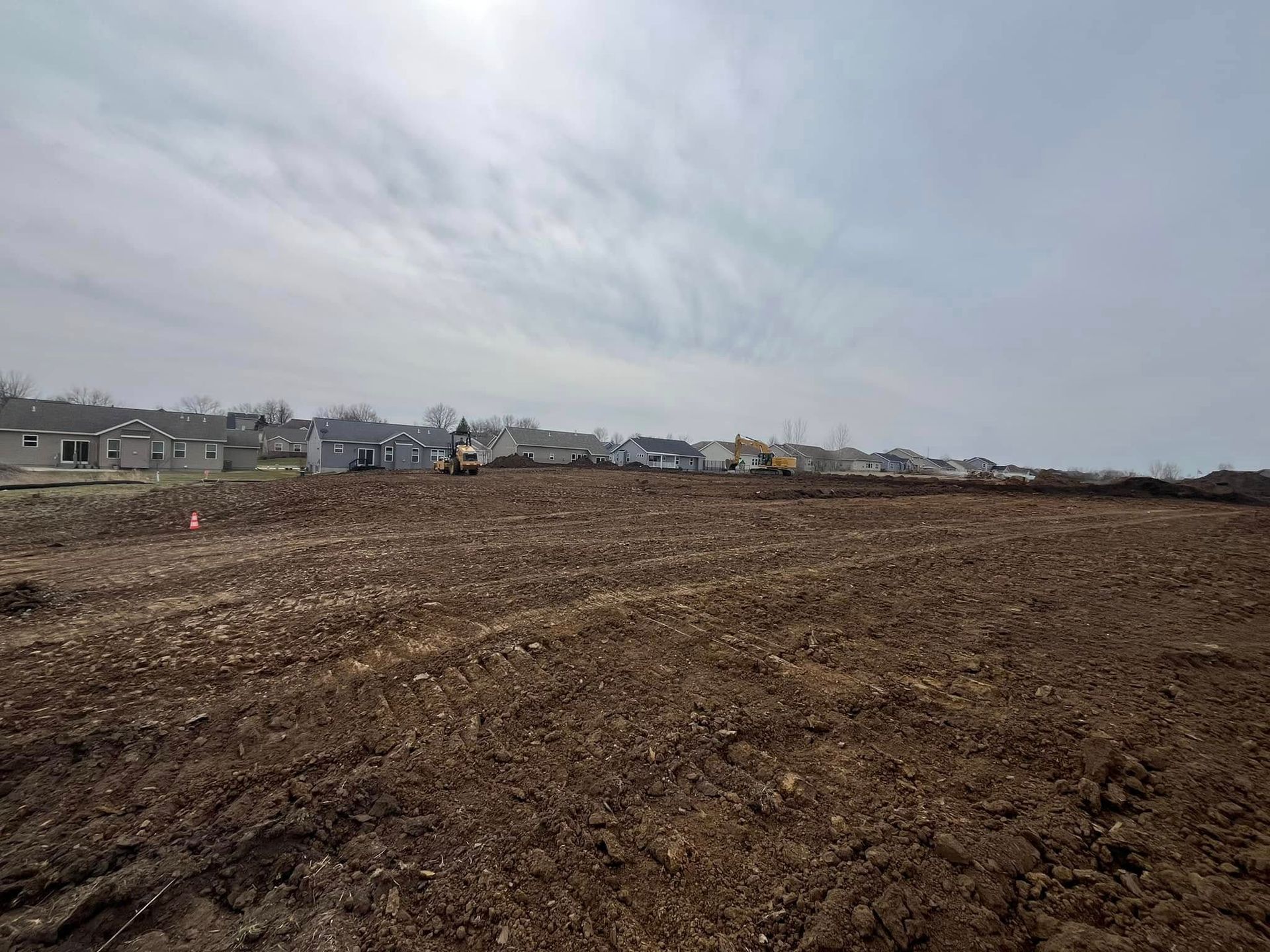A large dirt field with houses in the background and a cloudy sky.
