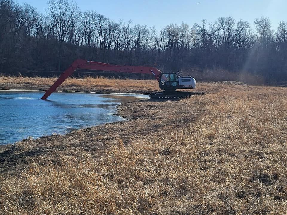 A large excavator is working on a lake in a field.