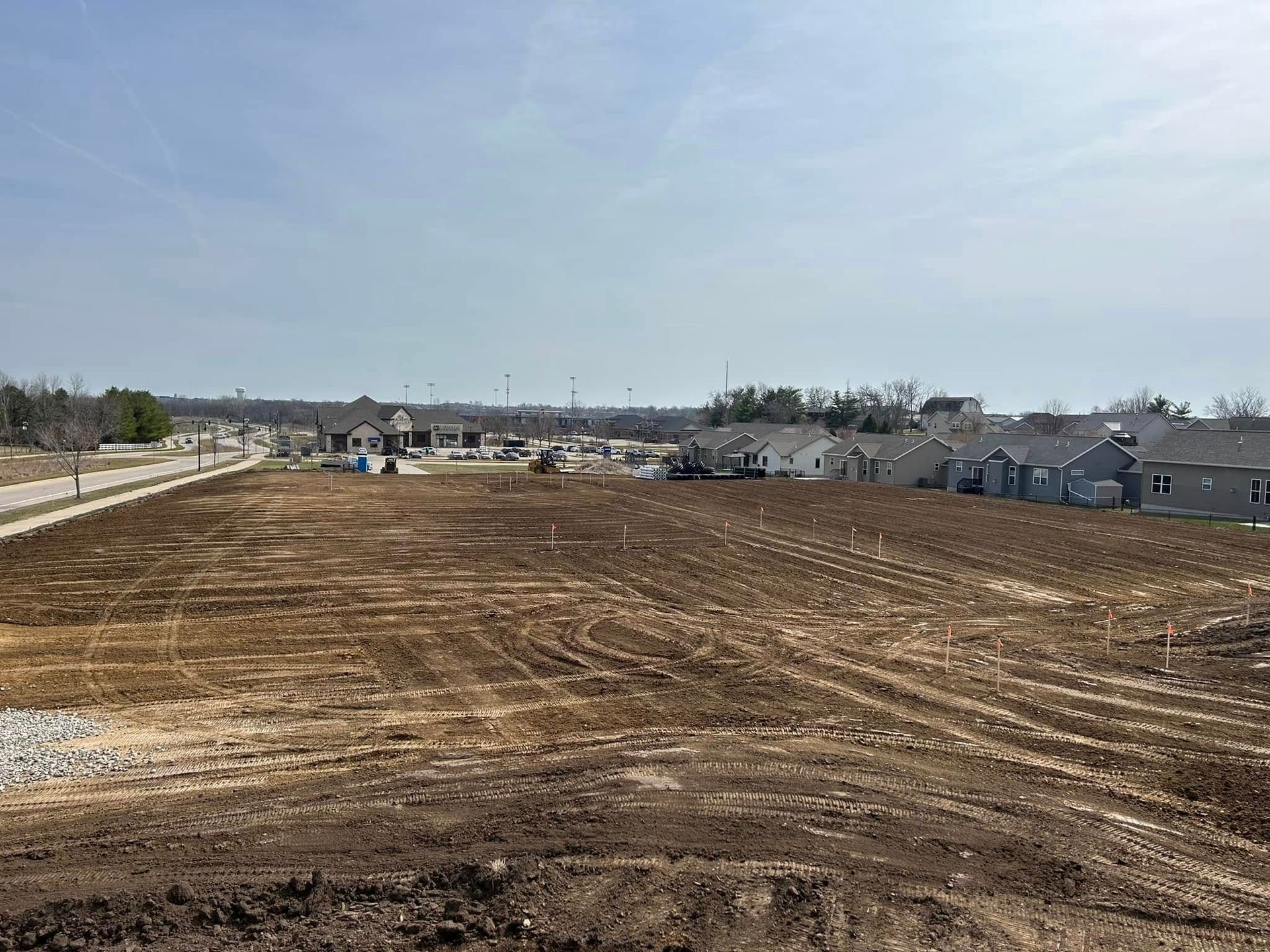 A large dirt field with a row of houses in the background.
