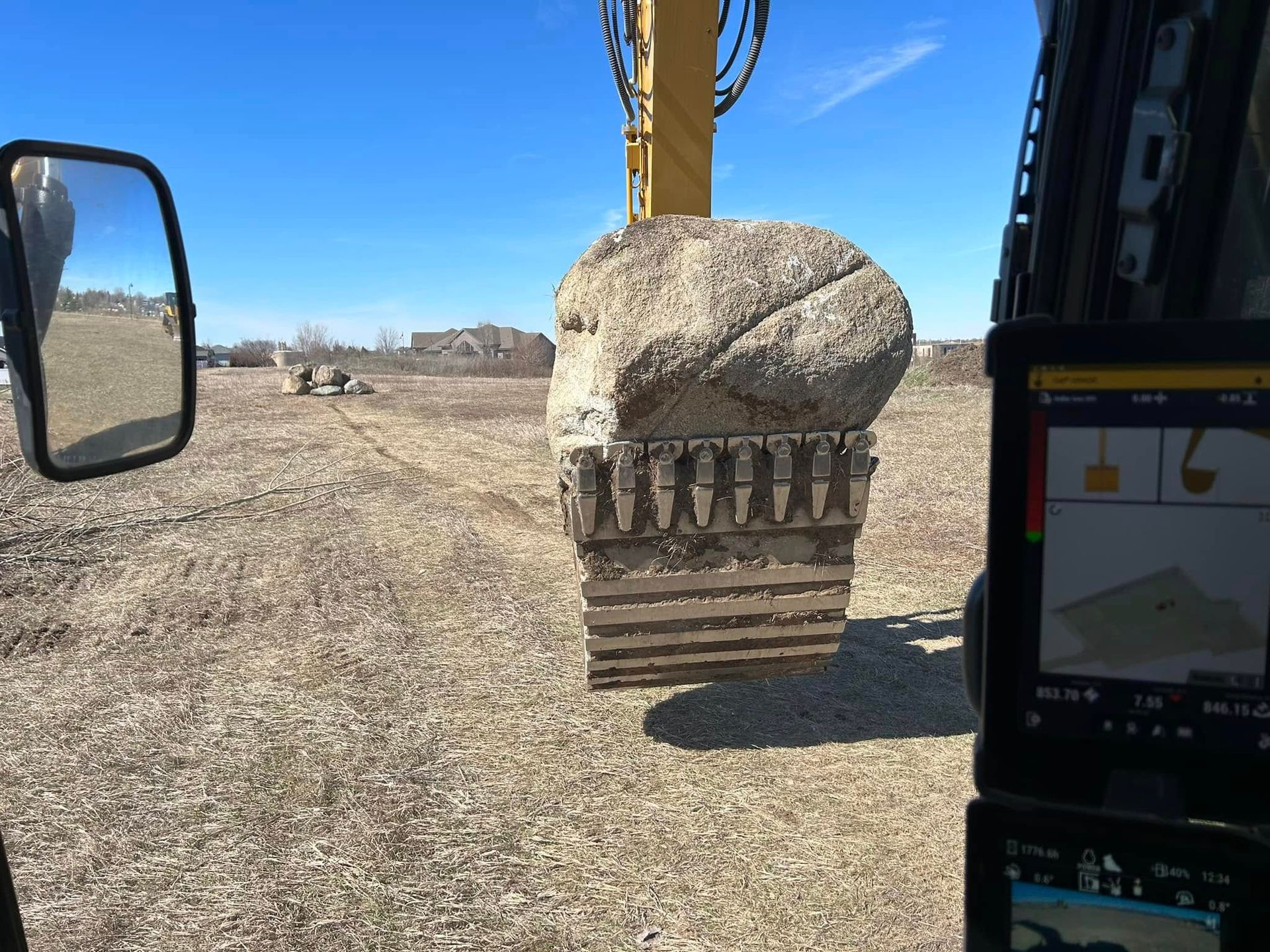 A large rock is being lifted by a bulldozer in a field