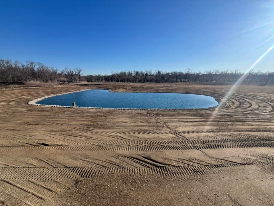 There is a large pond in the middle of a dirt field.
