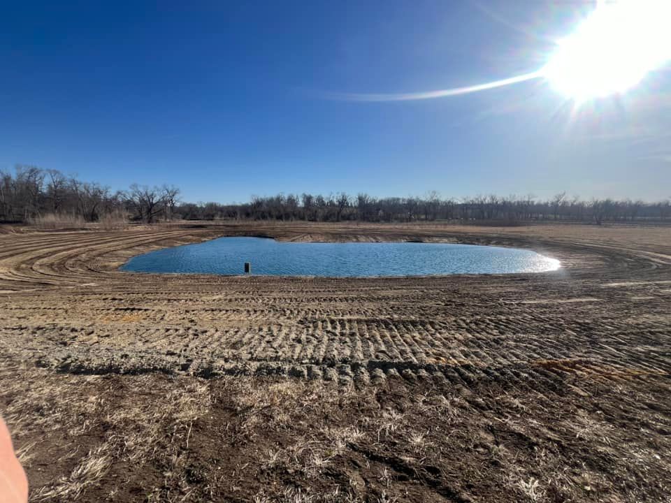 There is a small pond in the middle of a dirt field.