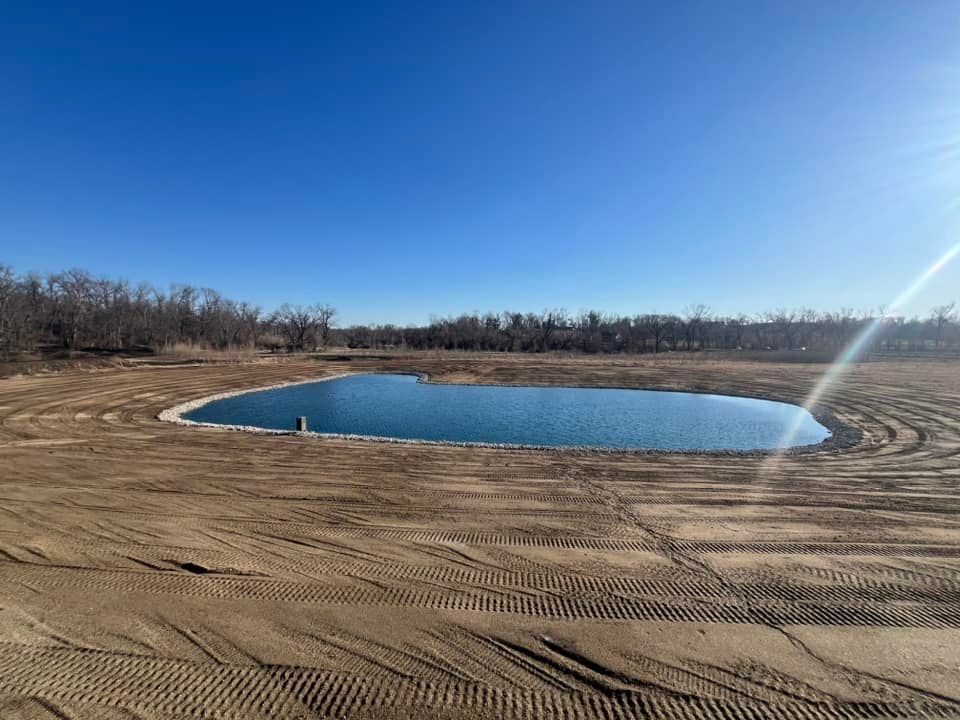 There is a large pond in the middle of a dirt field.