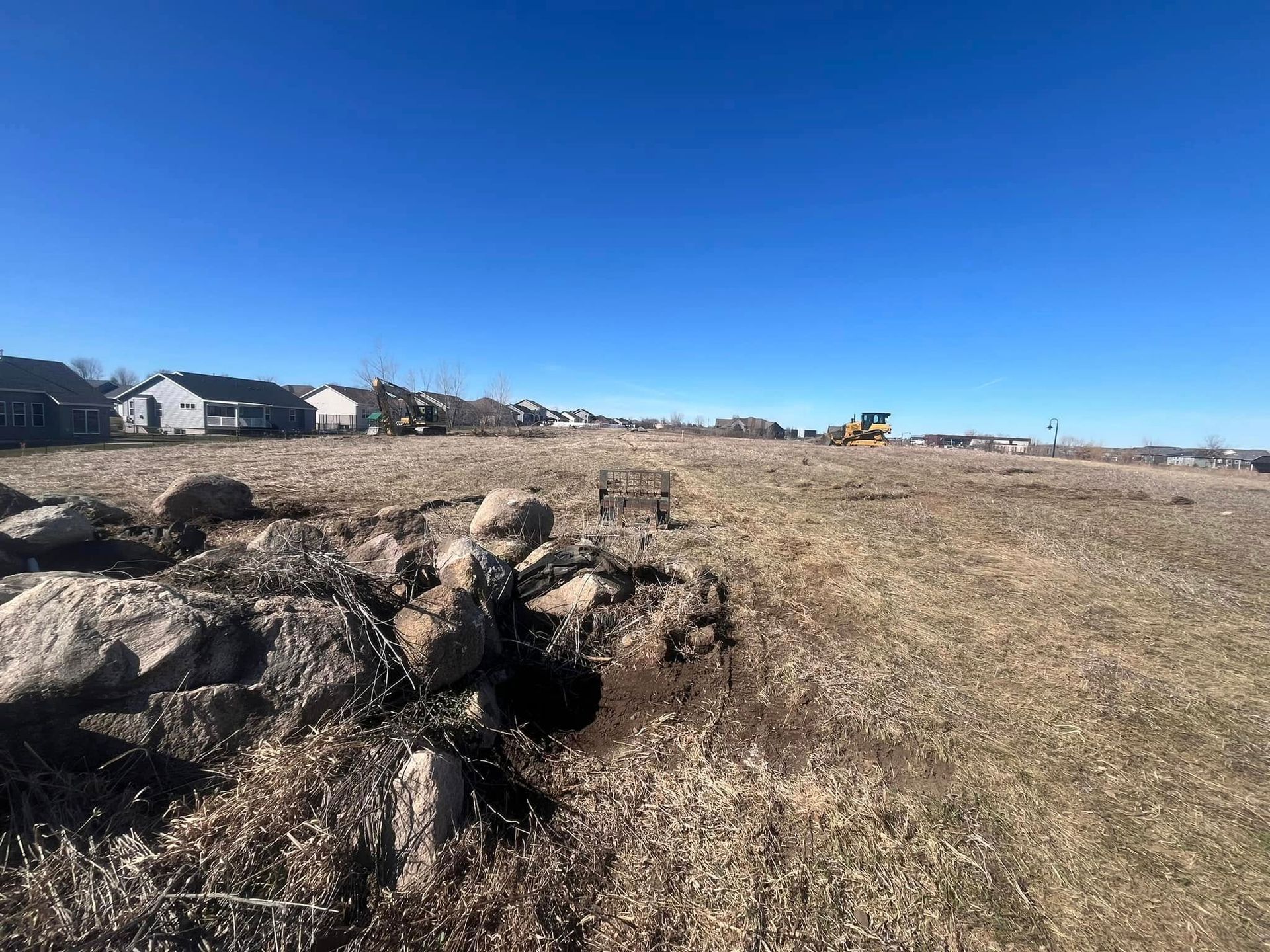 A large rock wall is sitting in the middle of a dry grass field.