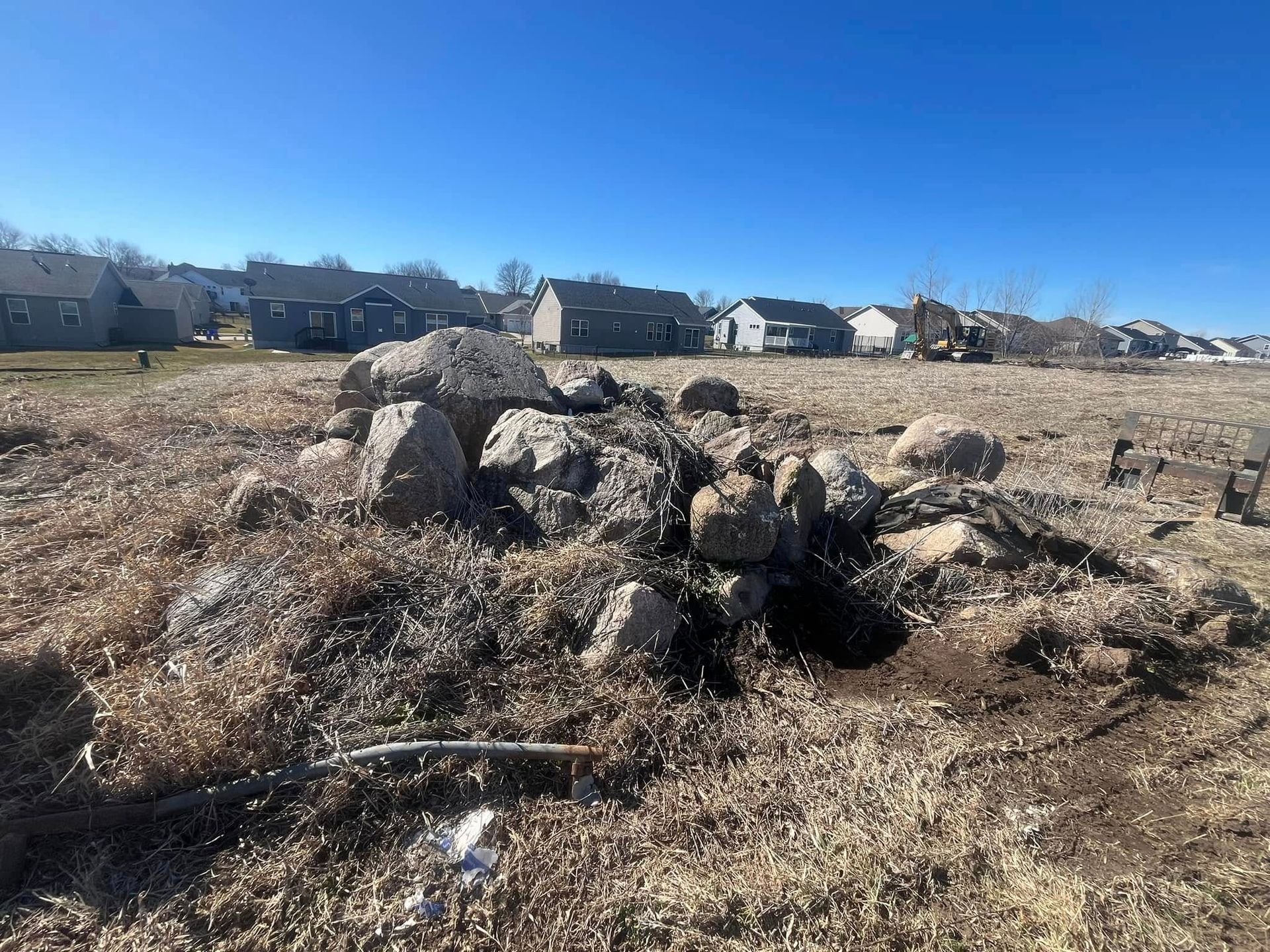 A pile of rocks in a field with houses in the background.