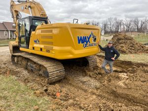 A man is standing in front of a large yellow excavator.