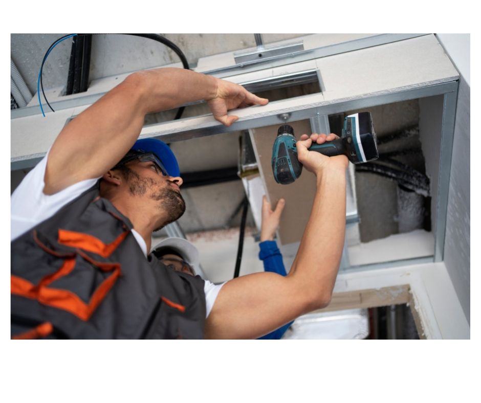 Man in work clothes uses a drill to install drywall on a ceiling.