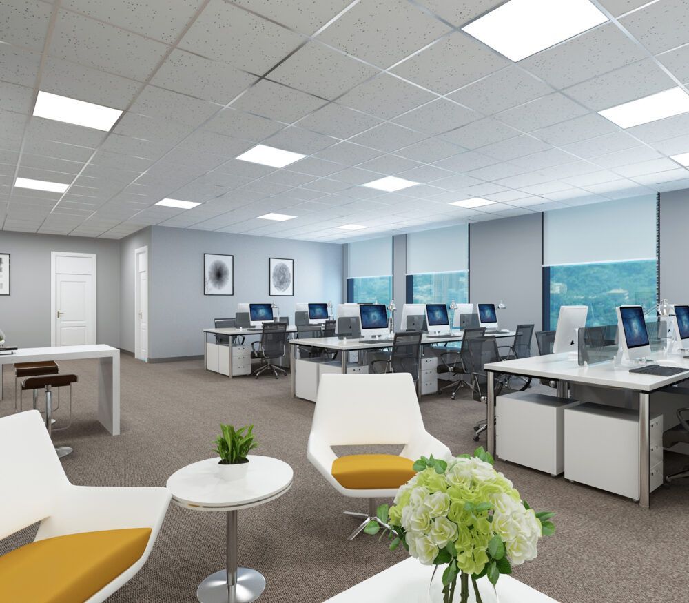 Modern office space with desks, chairs, and a lounge area with white furniture and plants.