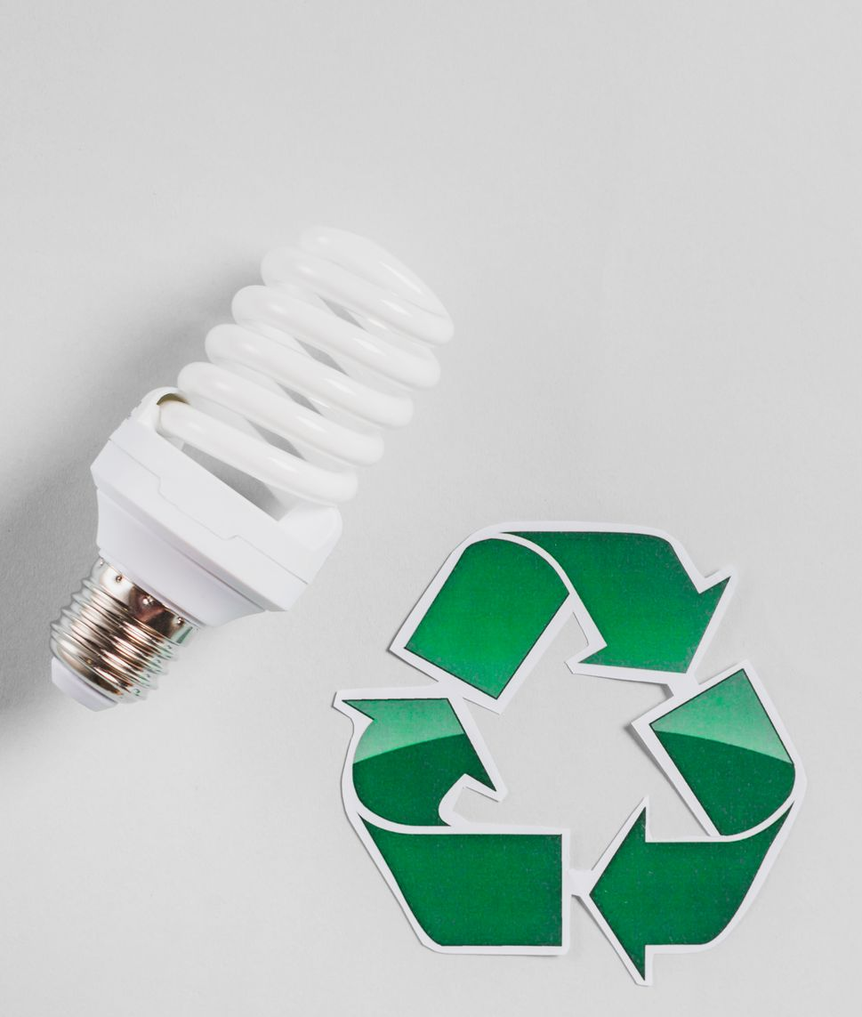 White energy-efficient light bulb next to a green recycling symbol, on a white background.