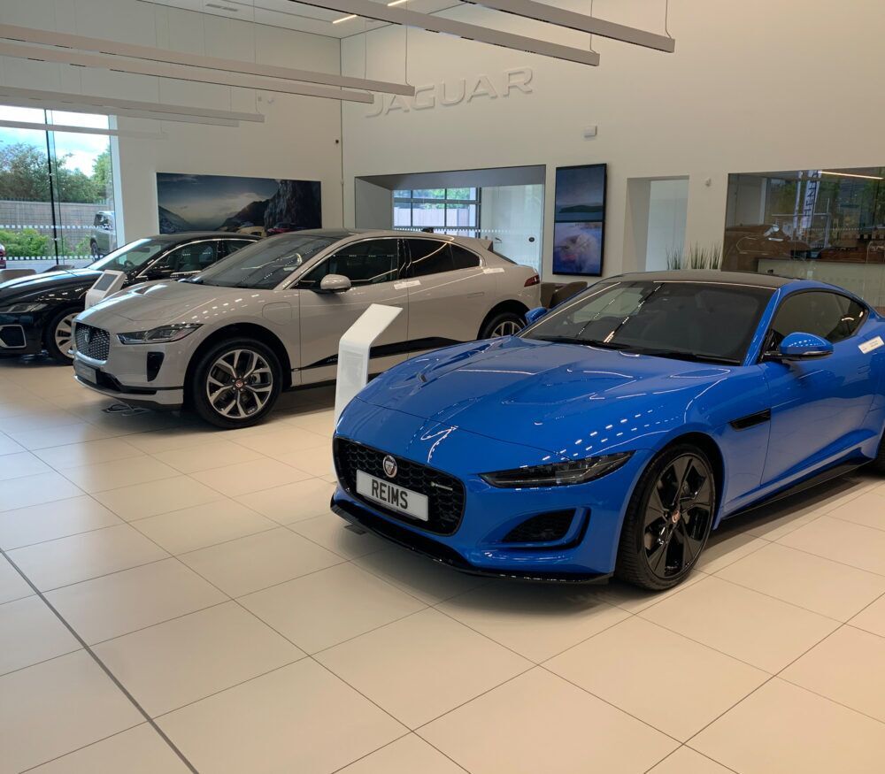 Blue Jaguar F-Type sports car on display in a showroom with other Jaguar models.