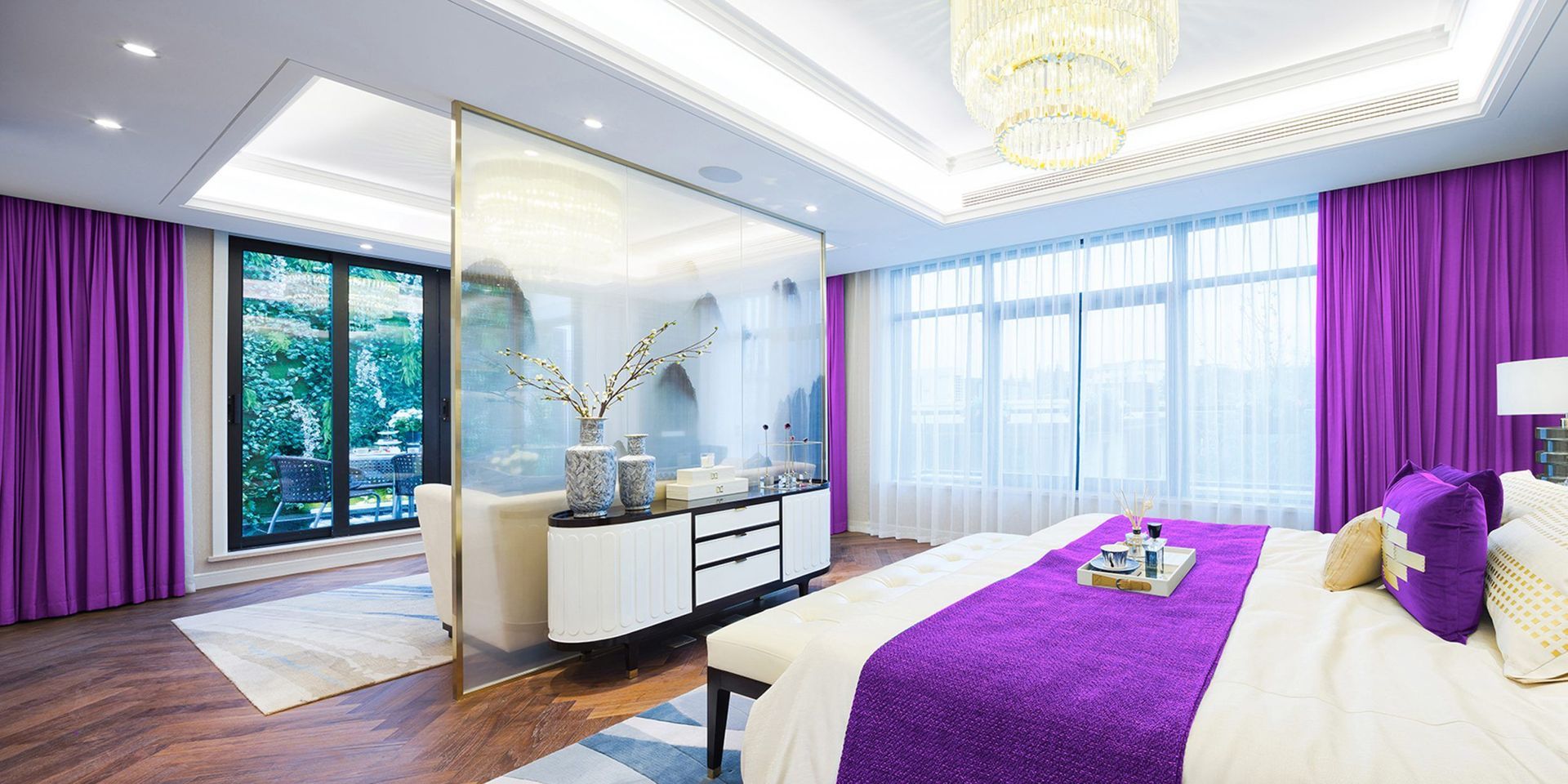 A modern bedroom with a purple color scheme. The bed is centered with purple bedding and curtains.