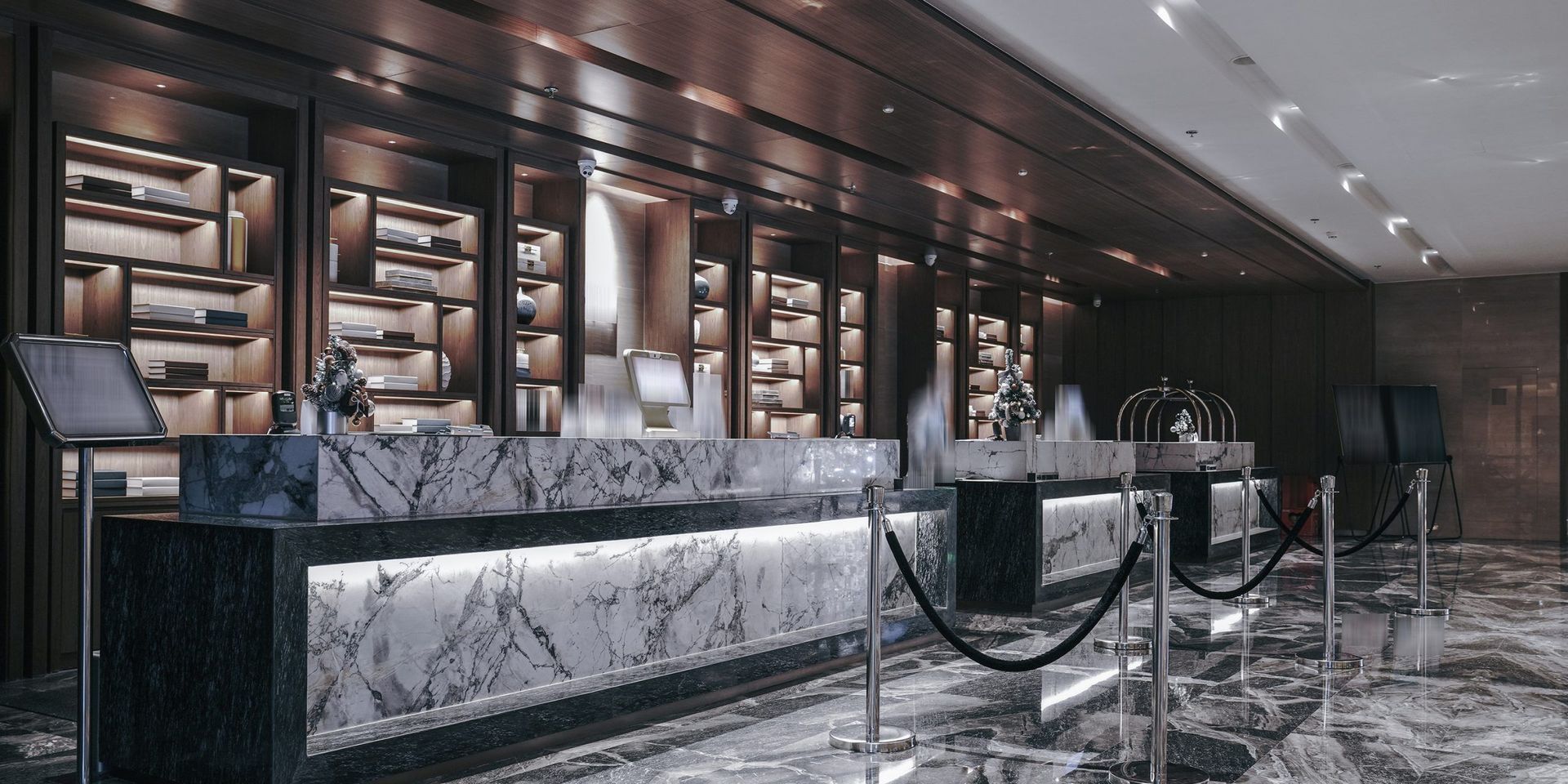 Hotel reception desk with marble countertop, dark wood shelves, and stanchions.