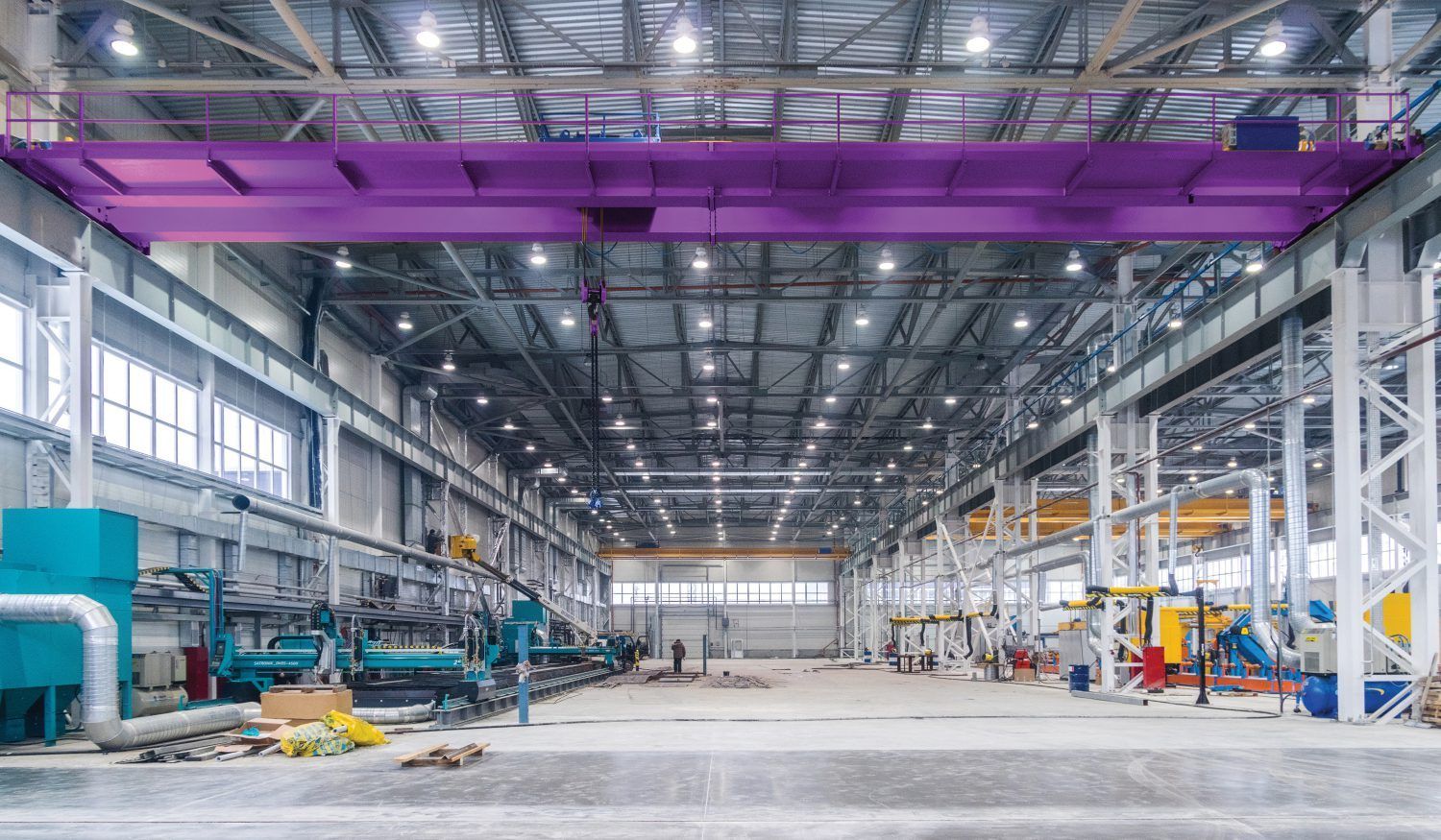 Large industrial warehouse with a purple overhead crane and various machinery.