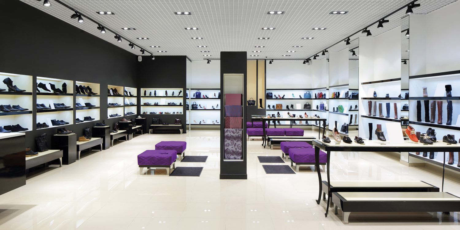 Shoe store interior with displays of shoes and purple ottomans, bright lighting.