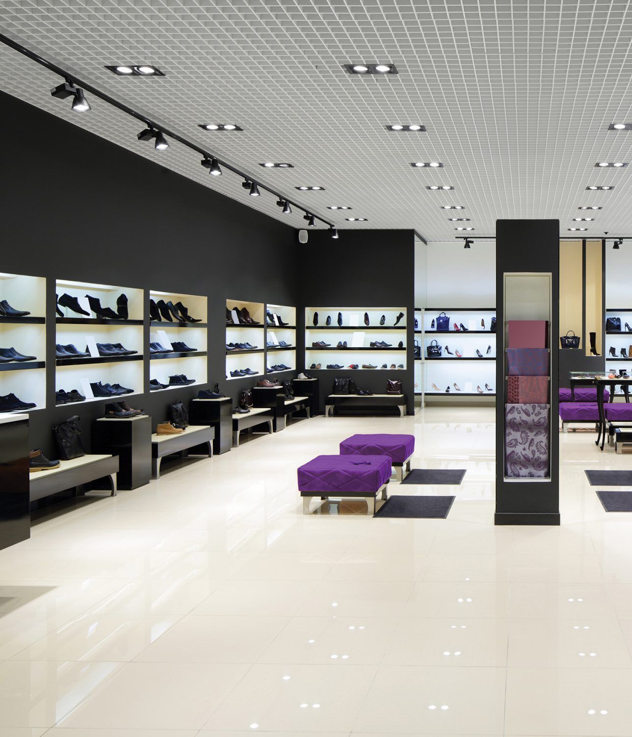 Shoe store interior with black walls, white floors, and purple seating. Shoes are displayed on shelves.