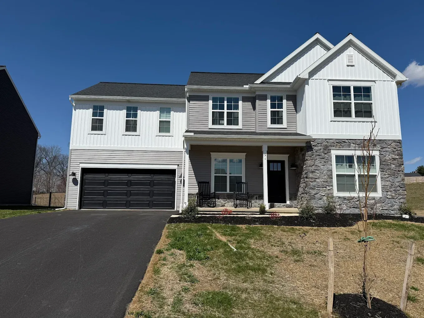 Two-story house with gray, white, and stone exterior, black garage door, and a paved driveway.