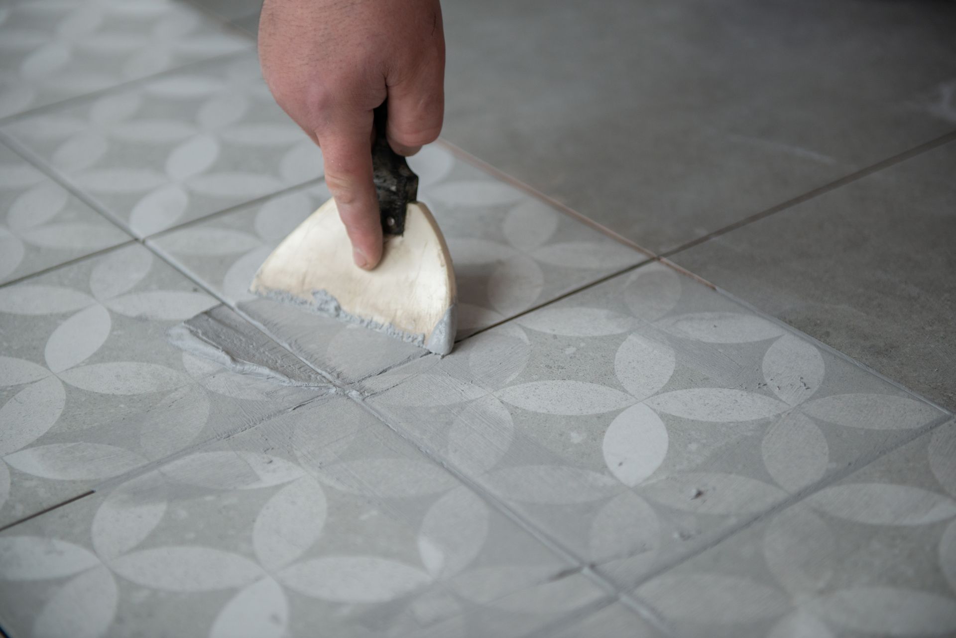 Hand using a trowel to apply grout to floor tile joints.