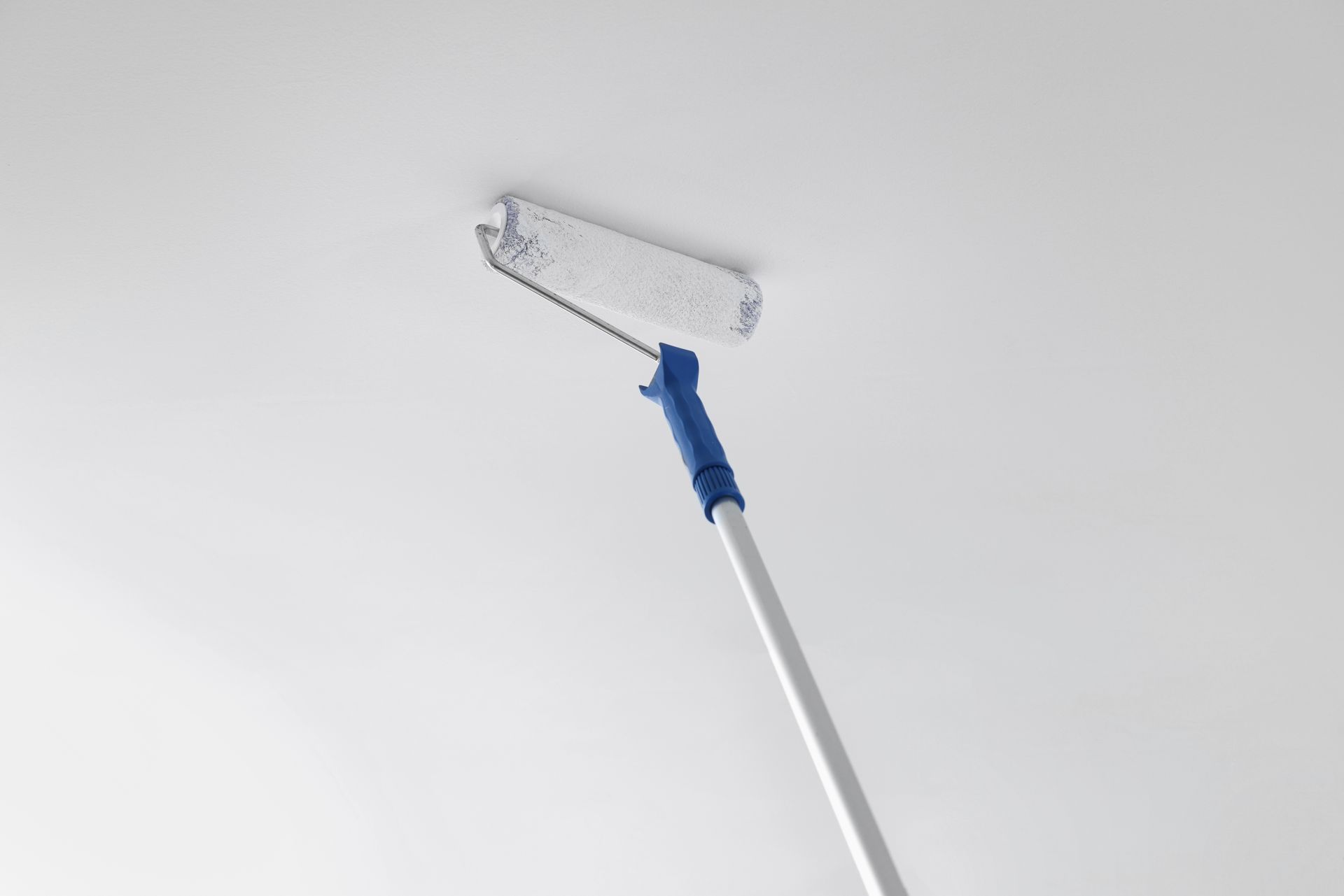 Paint roller with extension pole applying paint to a white ceiling.