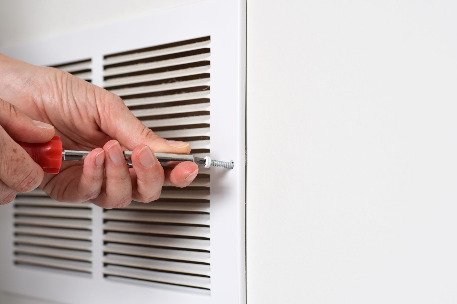 Person using a screwdriver on a white vent cover.