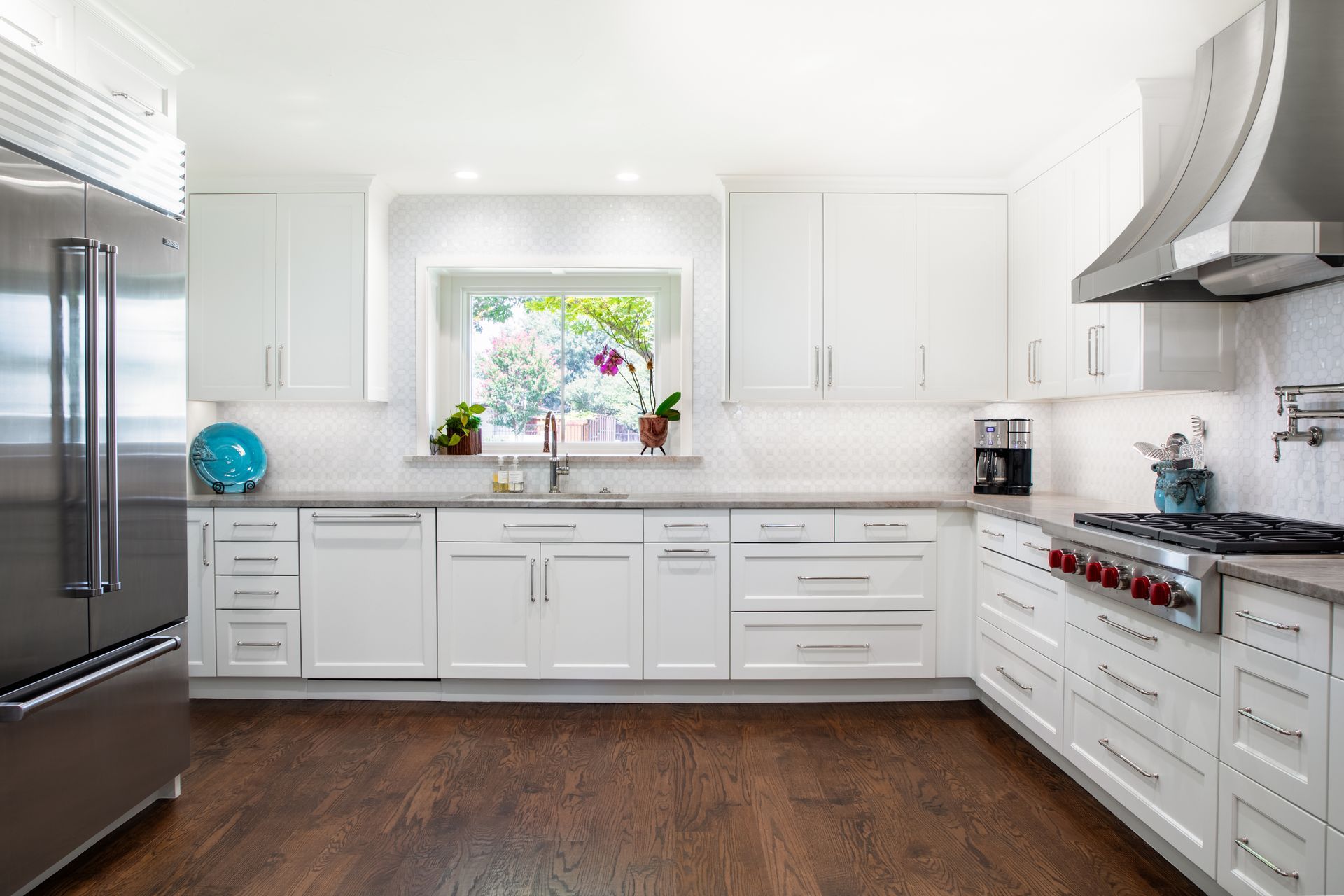 A bright kitchen with a stone accent wall, white cabinets, stainless steel appliances, and a marble-topped island.