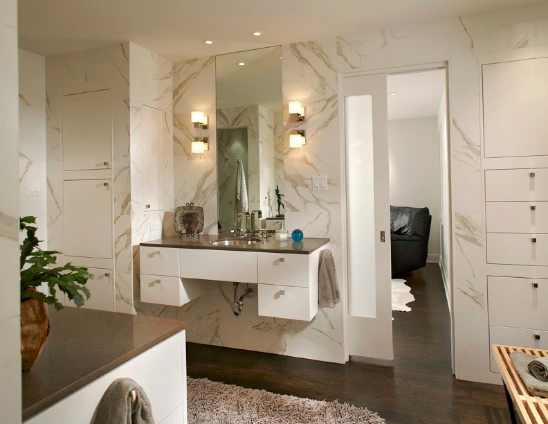 Modern bathroom with white and marble walls, floating vanity, large mirror, and open door to a bedroom.