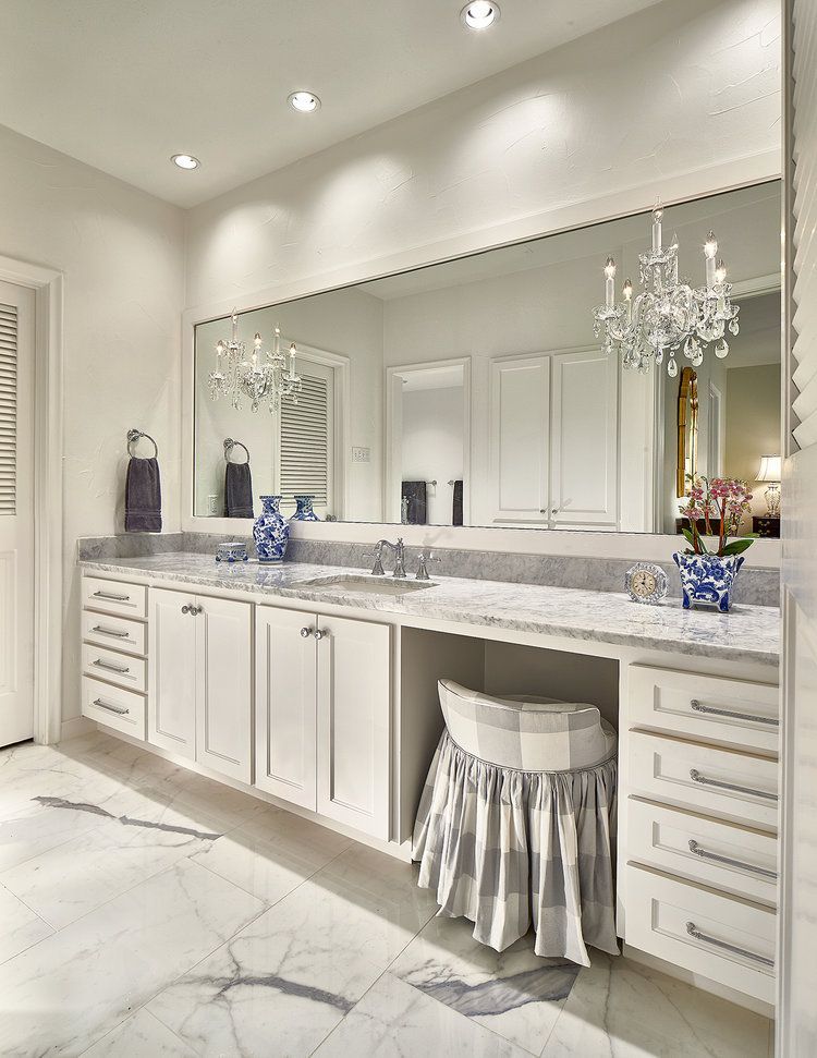 Elegant white bathroom with large mirror, granite countertop, drawers, and a skirted vanity stool.