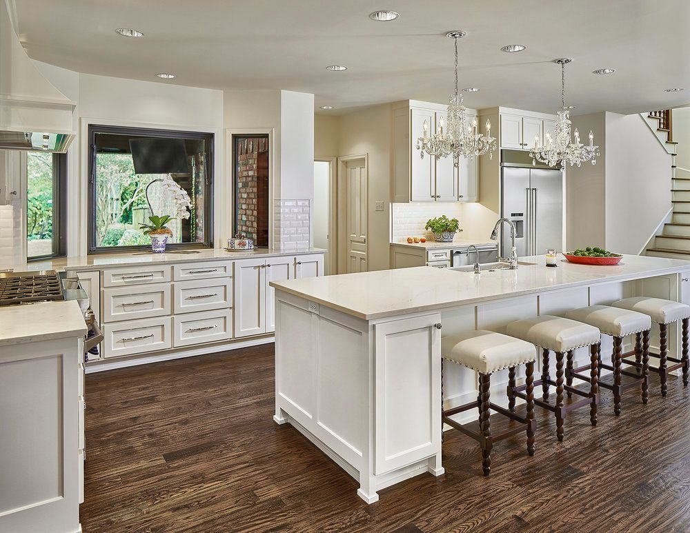 Elegant white kitchen with island, pendant lights, and bar stools; dark wood floors.