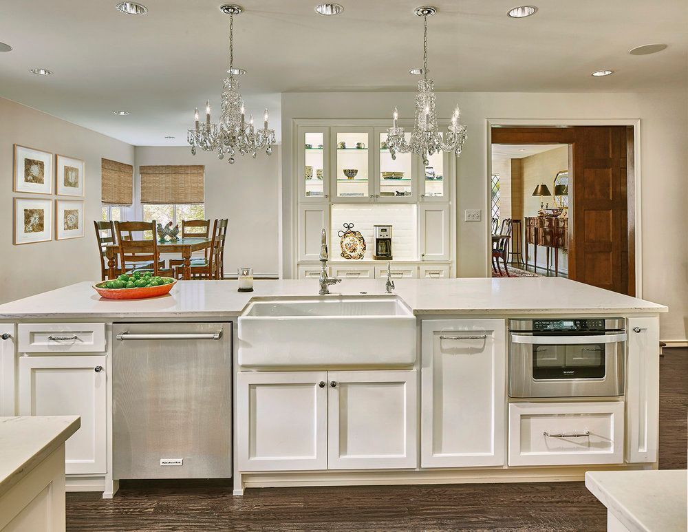 Spacious white kitchen with island, sink, dishwasher, and microwave. Dining area and built-in hutch in background.